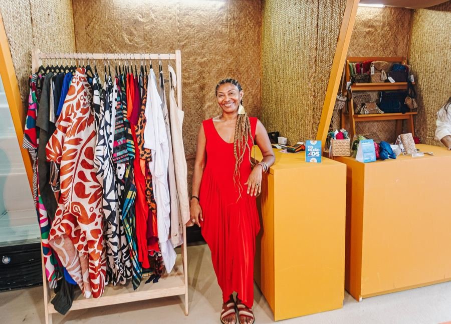 Empreendedora sorrindo em seu estande de moda na feira do Conexão ODS